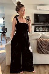woman wearing a black velvet wide-leg jumpsuit with a square neckline, standing in a bright living room