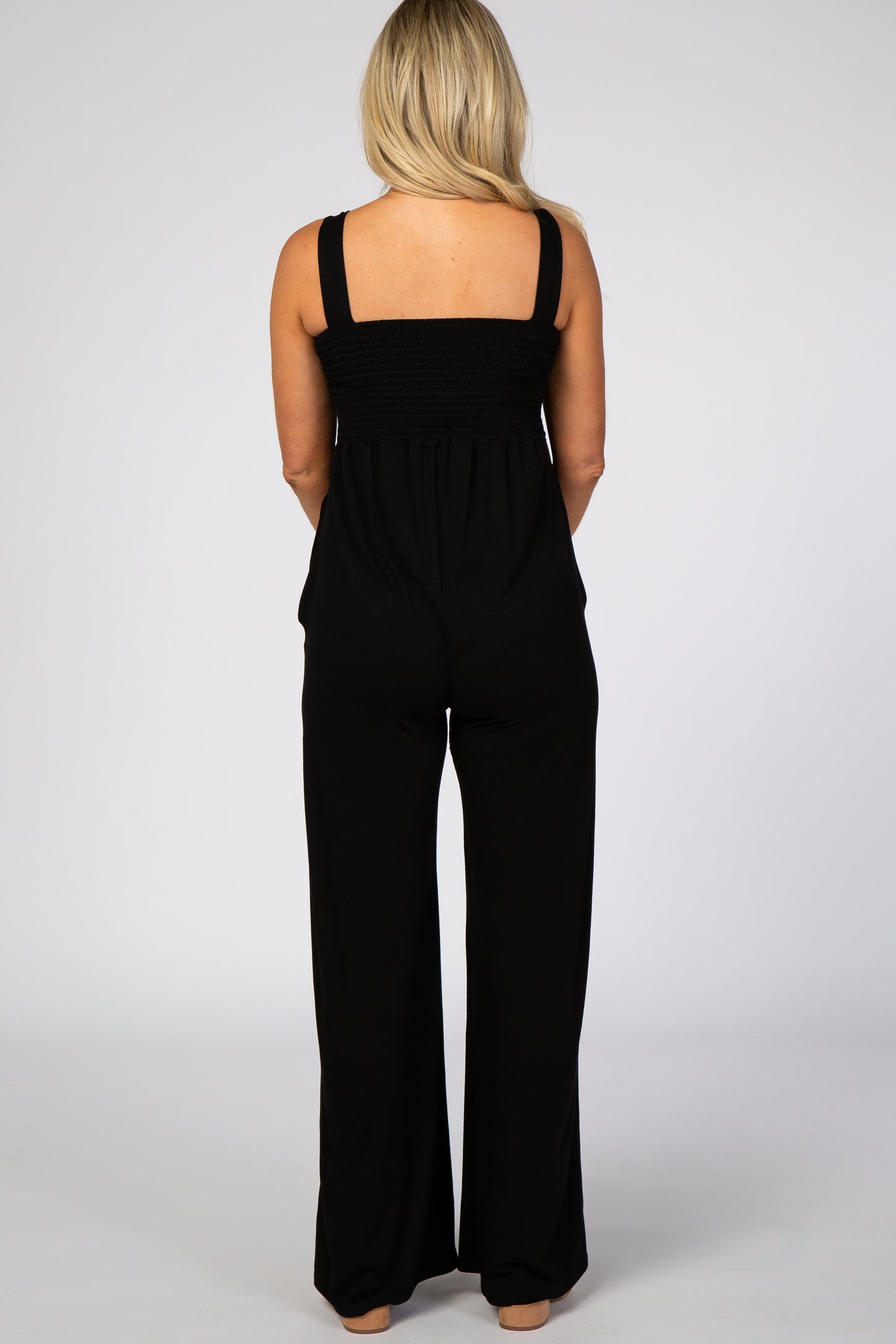 woman wearing a black maternity jumpsuit with a smocked bodice and wide leg pants, shown from the back