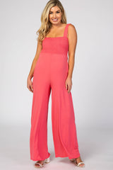 woman wearing a coral pink maternity jumpsuit with smocked bodice and wide-legged pants, model poses smiling