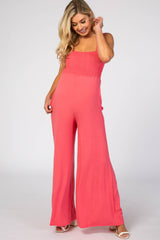 blonde woman wearing a coral pink smocked wide leg maternity jumpsuit with pockets