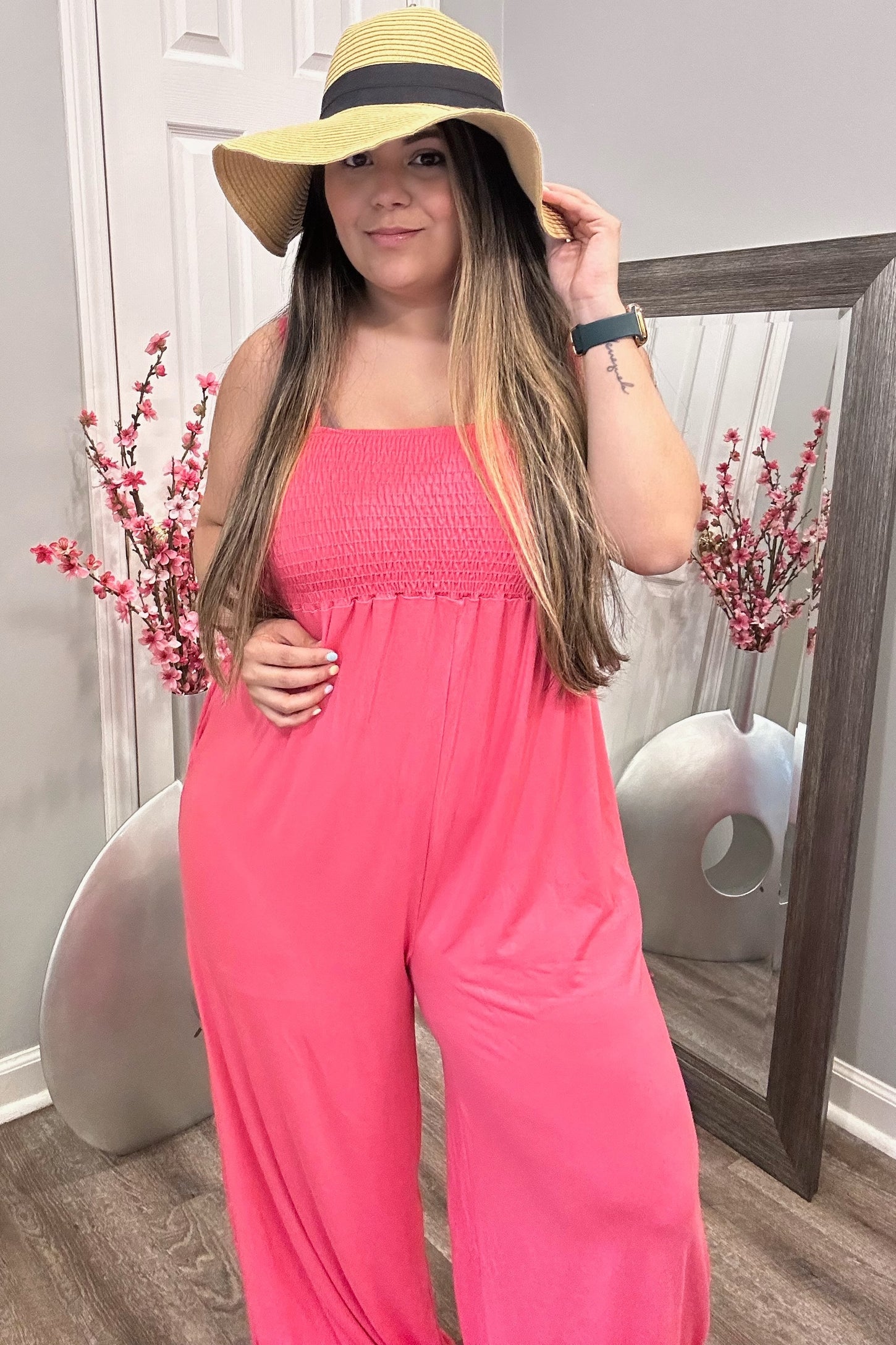 woman wearing a vibrant pink smocked jumpsuit and a wide-brimmed straw hat