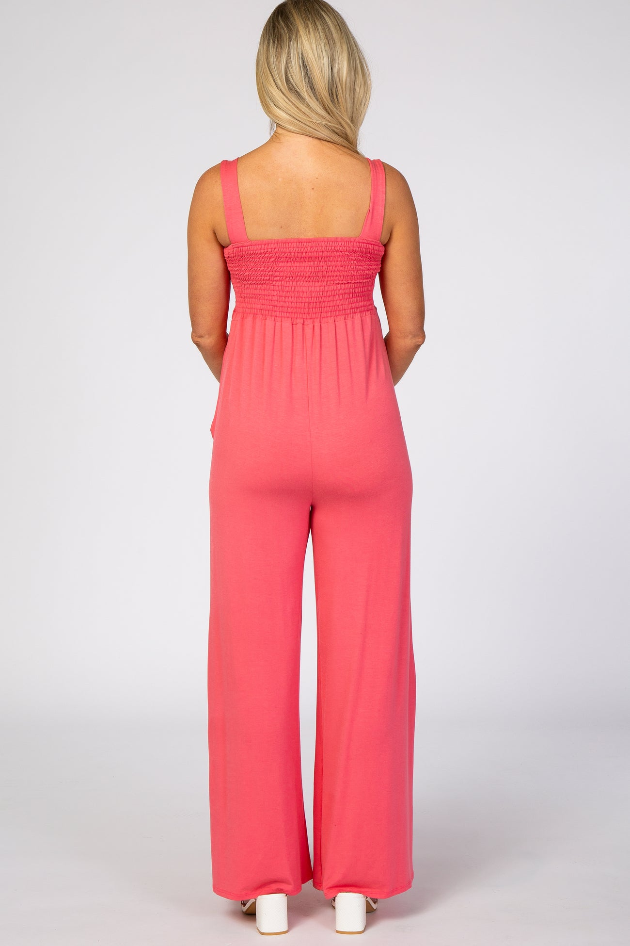 woman wearing a coral long dressy maternity jumpsuit with wide legs and smocked back detail