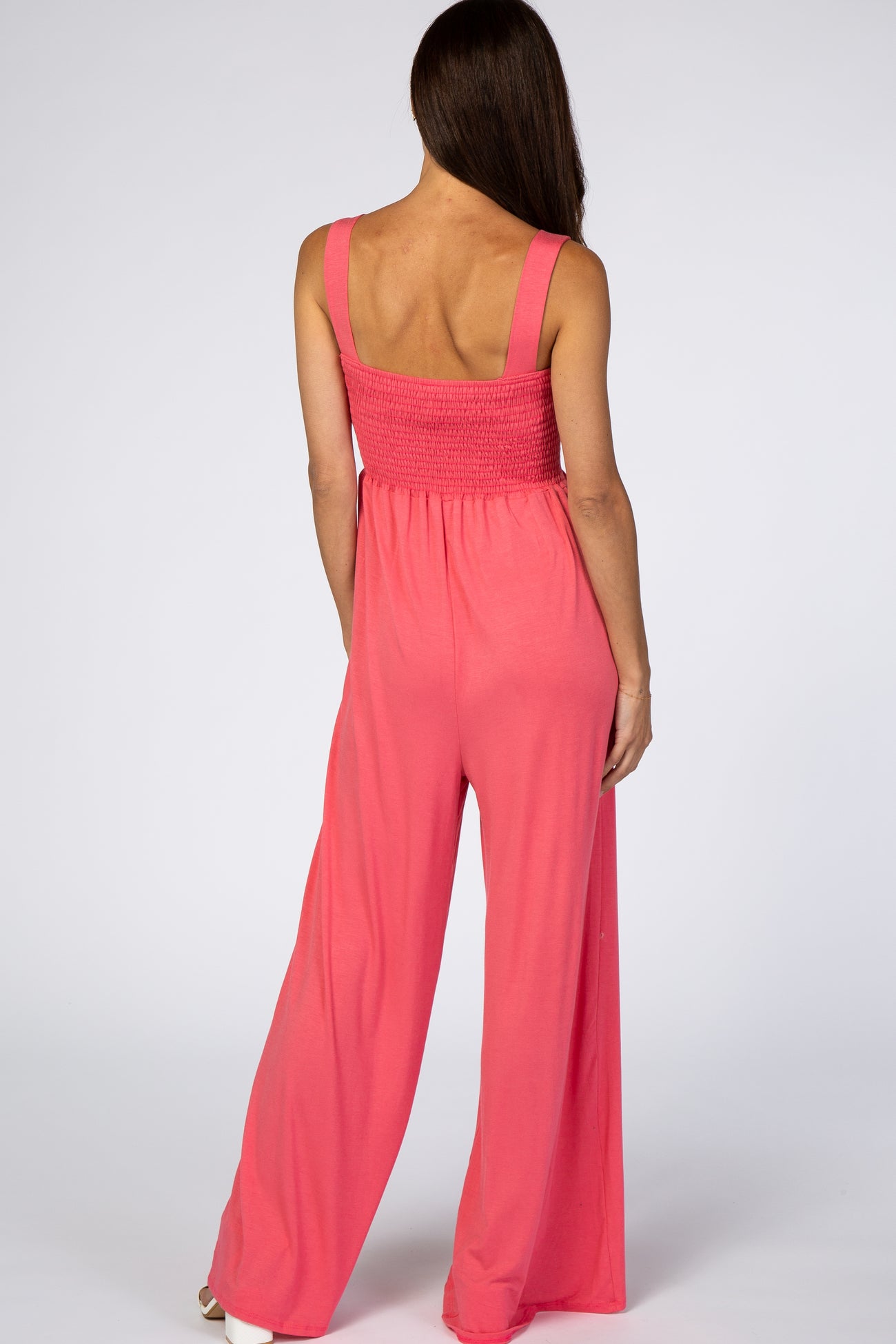 woman wearing a coral pink smocked back jumpsuit with wide-leg pants