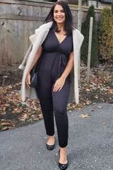 woman wearing a black jumpsuit with a wrap design and a grey faux fur coat, paired with black heels and a small handbag