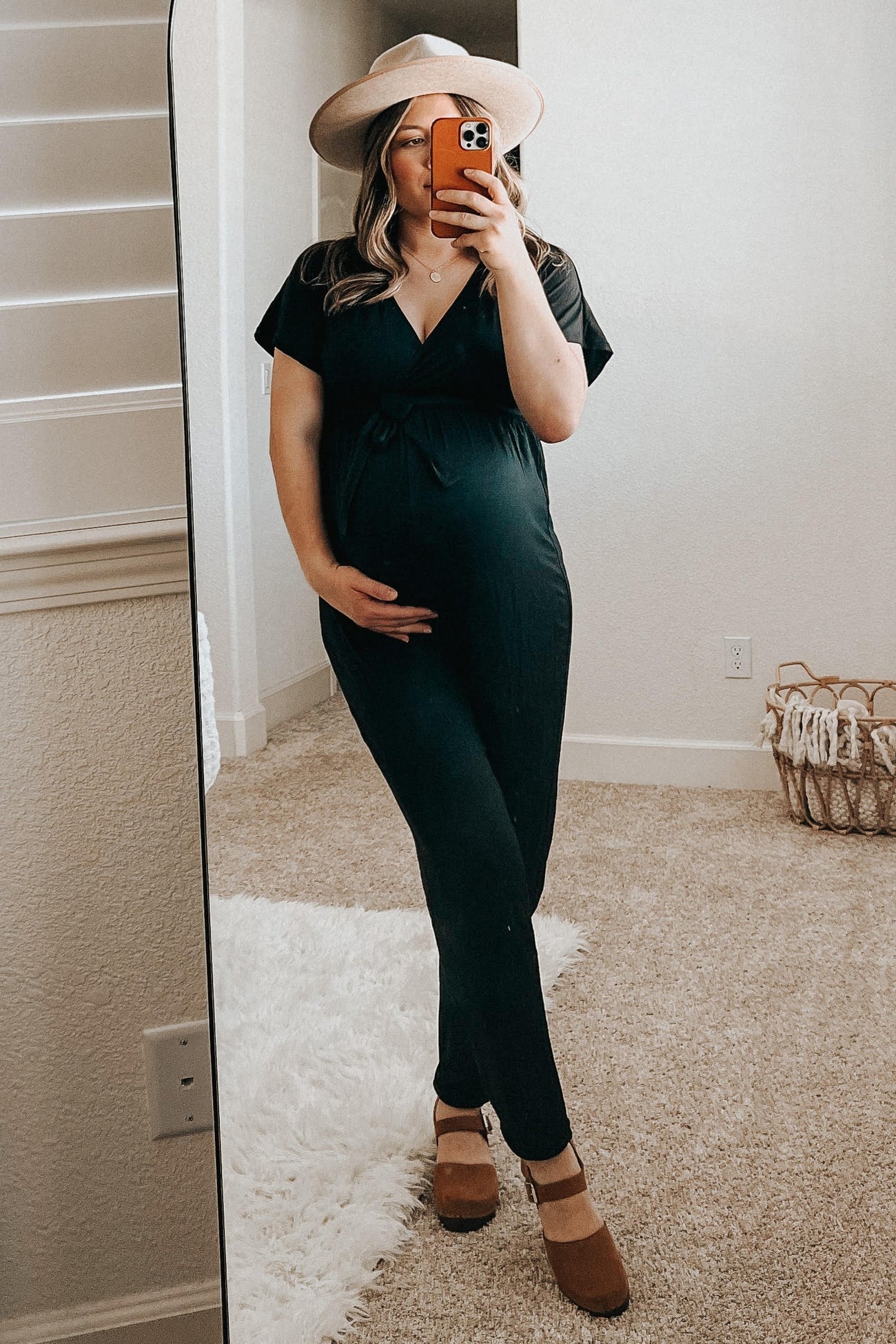 woman wearing a black maternity jumpsuit and holding her baby bump while standing in front of a mirror