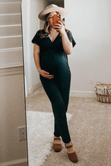 woman wearing a black maternity jumpsuit and holding her baby bump while standing in front of a mirror