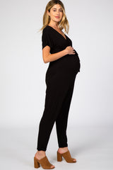 woman wearing a black maternity jumpsuit and showing her baby bump while standing sideways