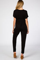 woman wearing a black maternity jumpsuit with short sleeves and a relaxed fit from the back