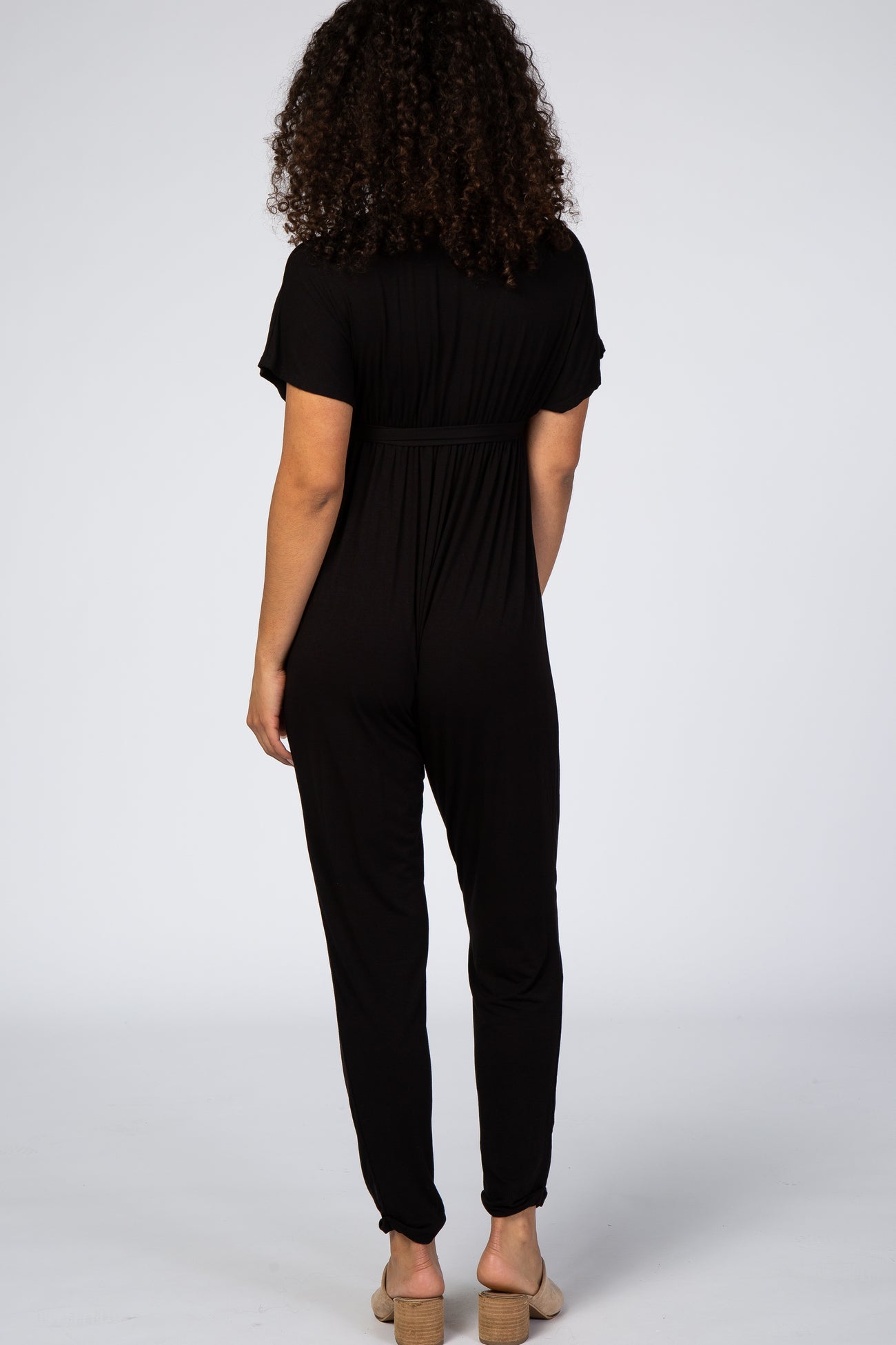 woman wearing a black short sleeve jumpsuit with a gathered waist and tapered legs, shown from the back