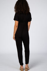 woman wearing a black short sleeve jumpsuit with a gathered waist and tapered legs, shown from the back