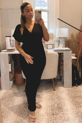 woman wearing a black v-neck jumpsuit with short sleeves and a fitted silhouette, standing in front of a desk