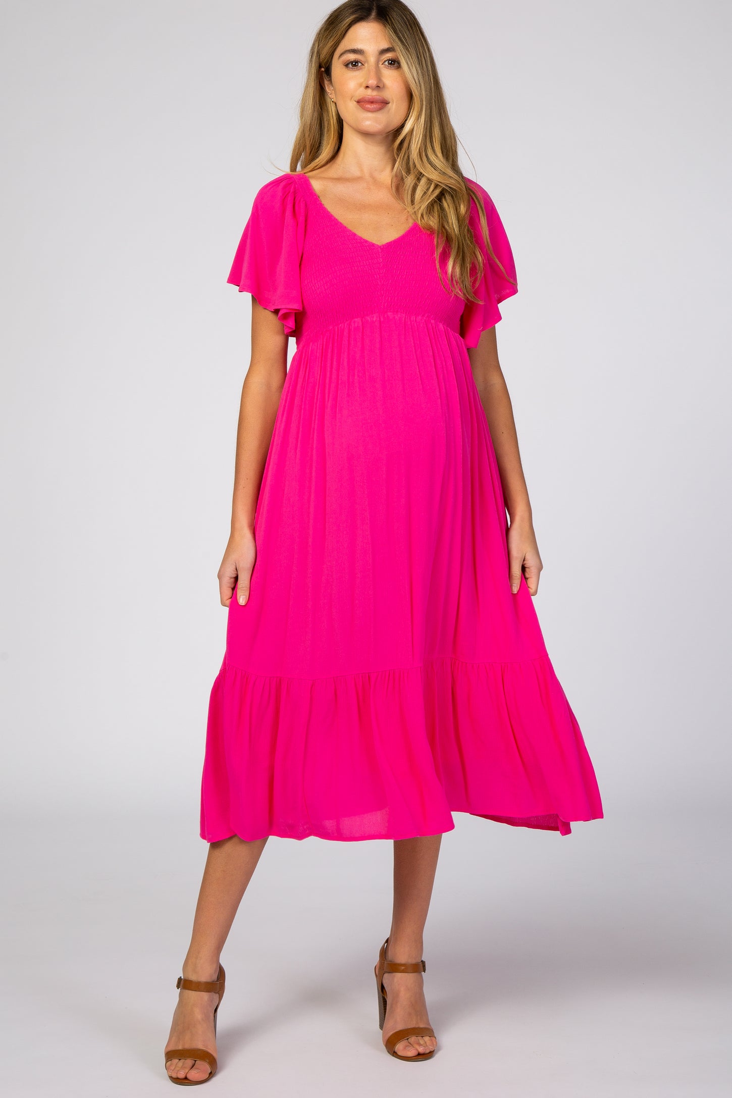 woman wearing a bright pink short sleeve maternity dress with a tiered skirt and a v-neckline, showing her baby bump
