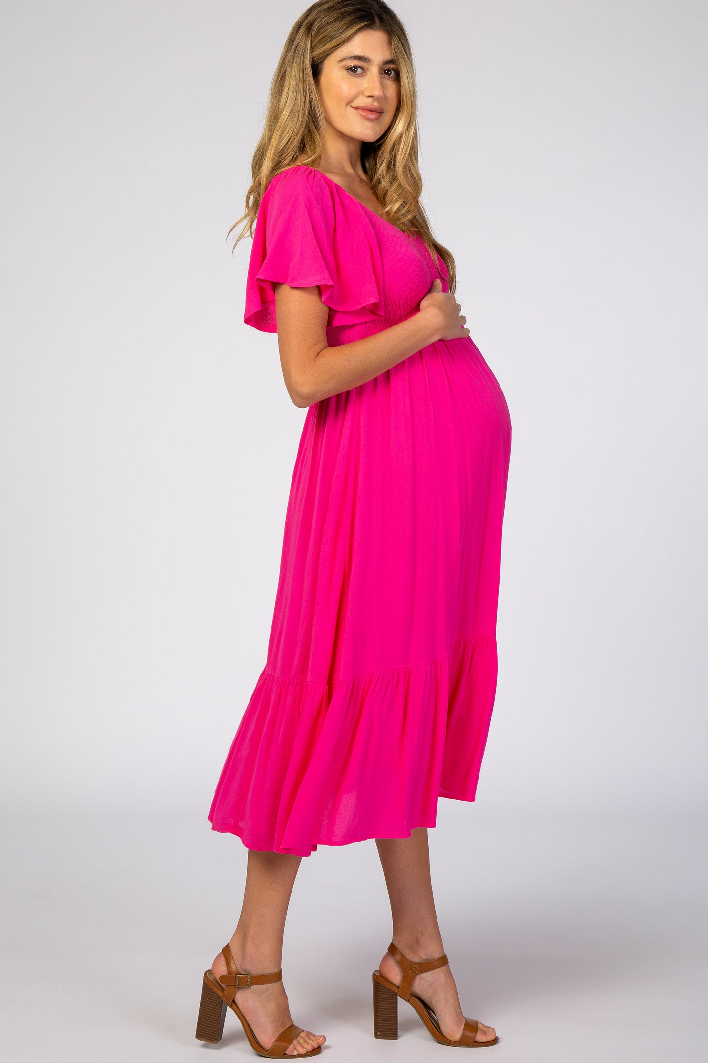 woman wearing a bright pink maternity dress with flutter sleeves and a tiered hem, cradling her baby bump