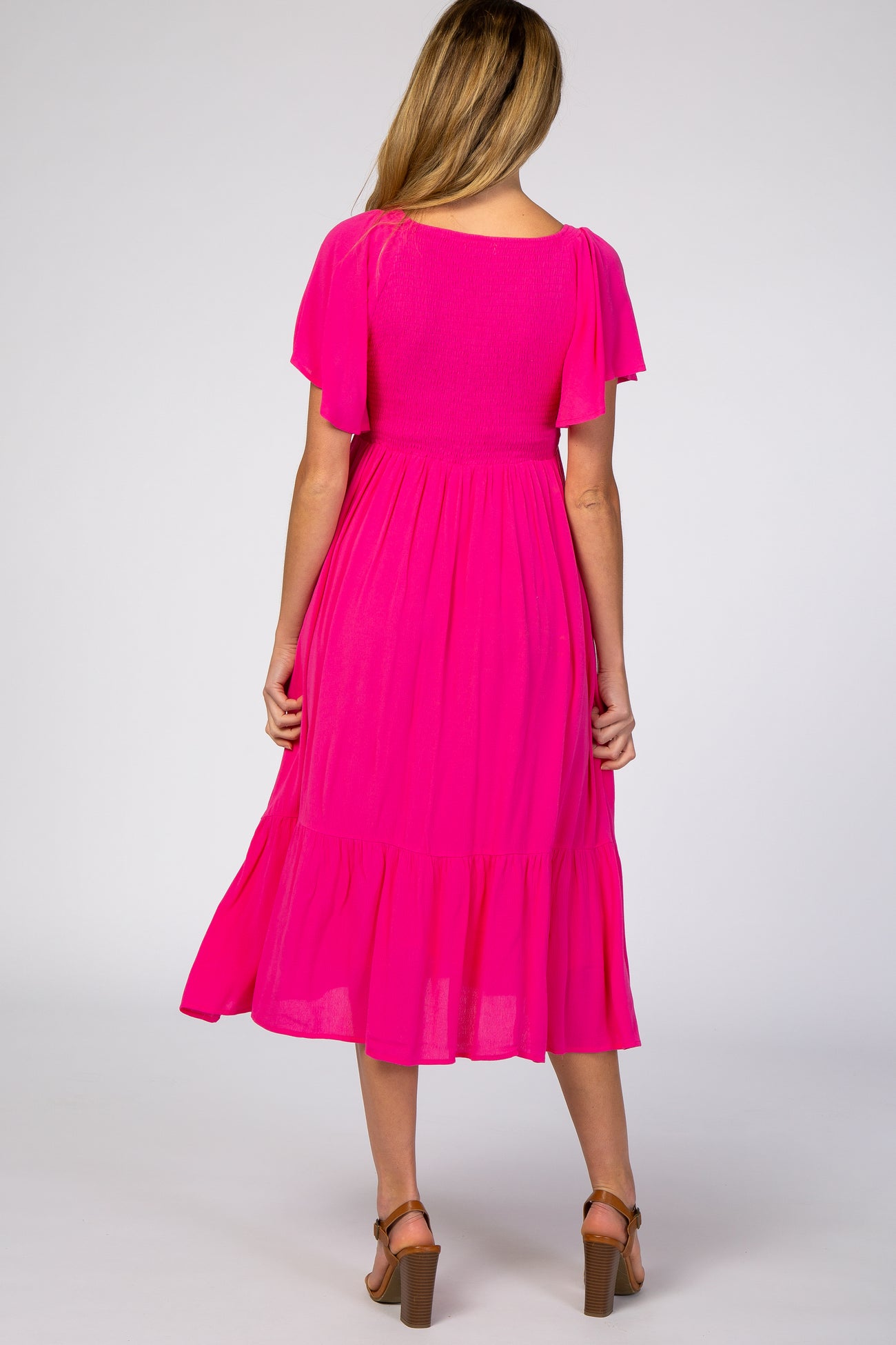 woman wearing a bright pink maternity dress with flutter sleeves and a tiered hem, showing the back view