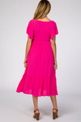 woman wearing a bright pink maternity dress with flutter sleeves and a tiered hem, showing the back view