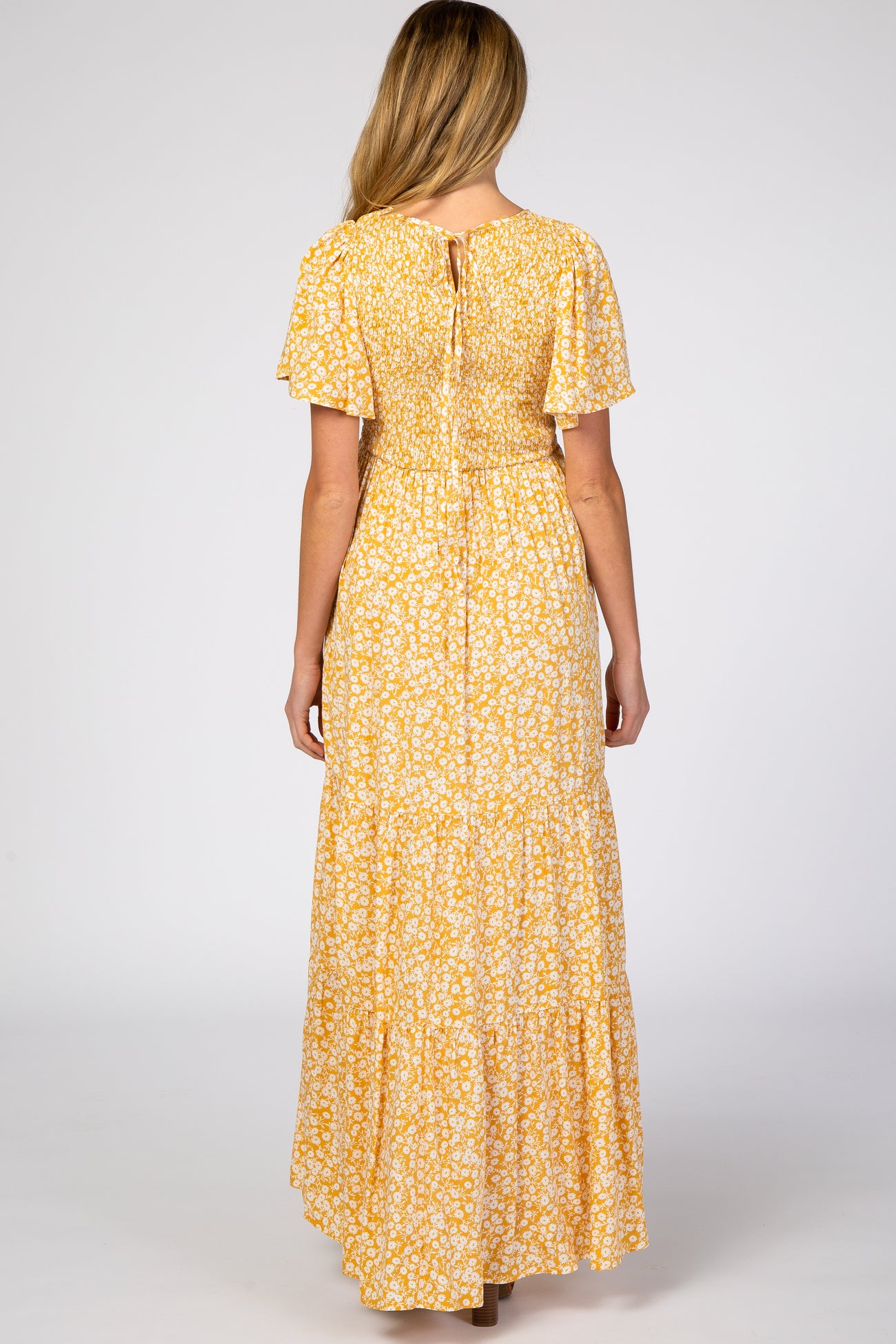 woman wearing a yellow floral maternity dress with short sleeves and a tiered skirt, seen from the back