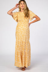 woman wearing a yellow floral maternity maxi dress with short sleeves and tiered skirt, standing with one hand on her hair