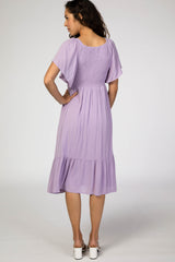 woman wearing a lavender short sleeve dress with a smocked bodice and ruffled hem, viewed from the back