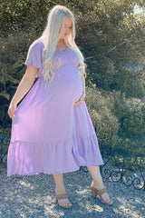 woman wearing a lavender maternity maxi dress with short sleeves and a tiered skirt, cradling her baby bump