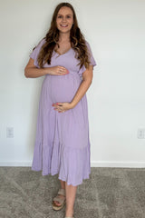 woman wearing a lilac maternity dress with short sleeves and a tiered skirt, highlighting her baby bump