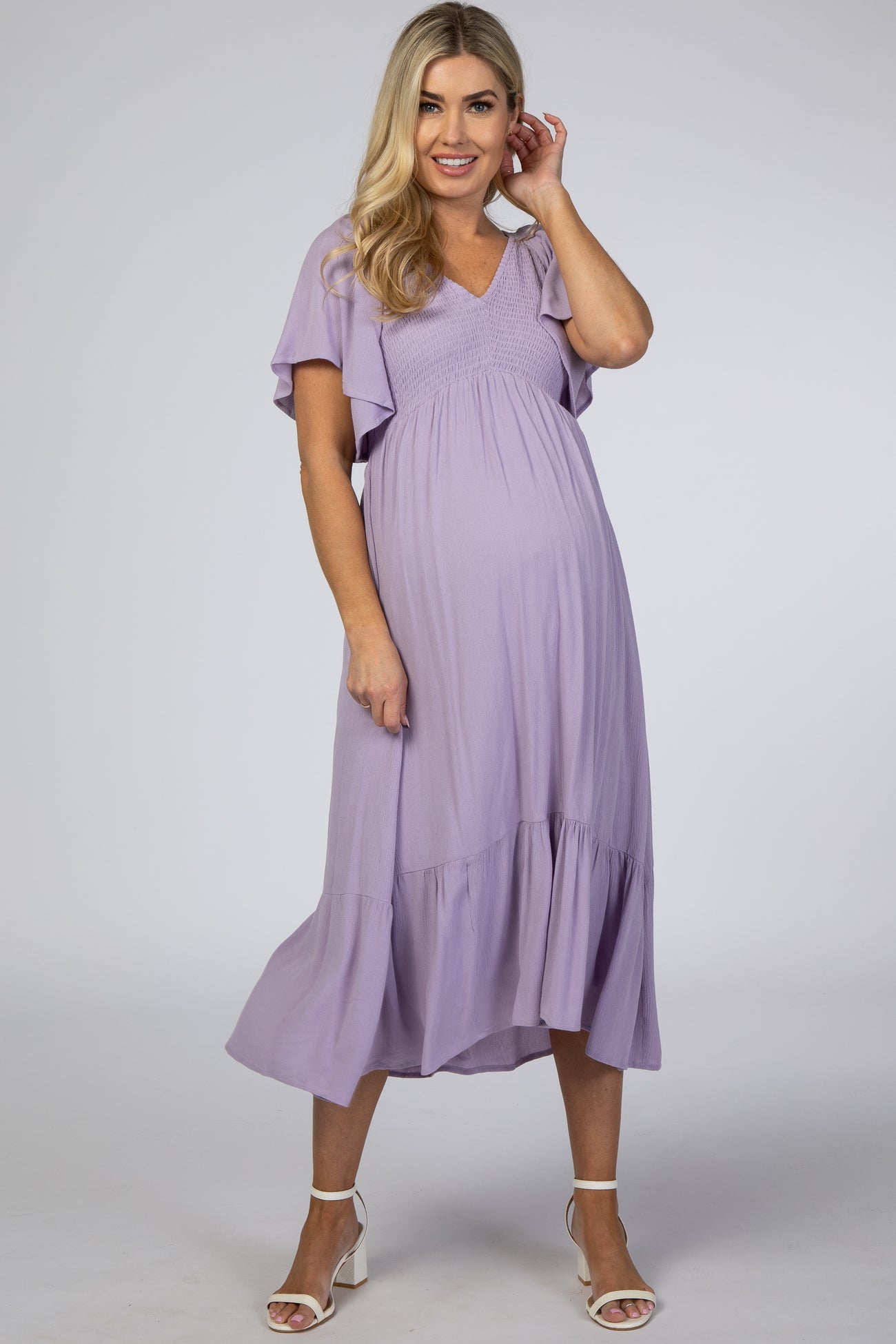 woman wearing a lavender maternity dress with flutter sleeves and a smocked bodice, showcasing her baby bump