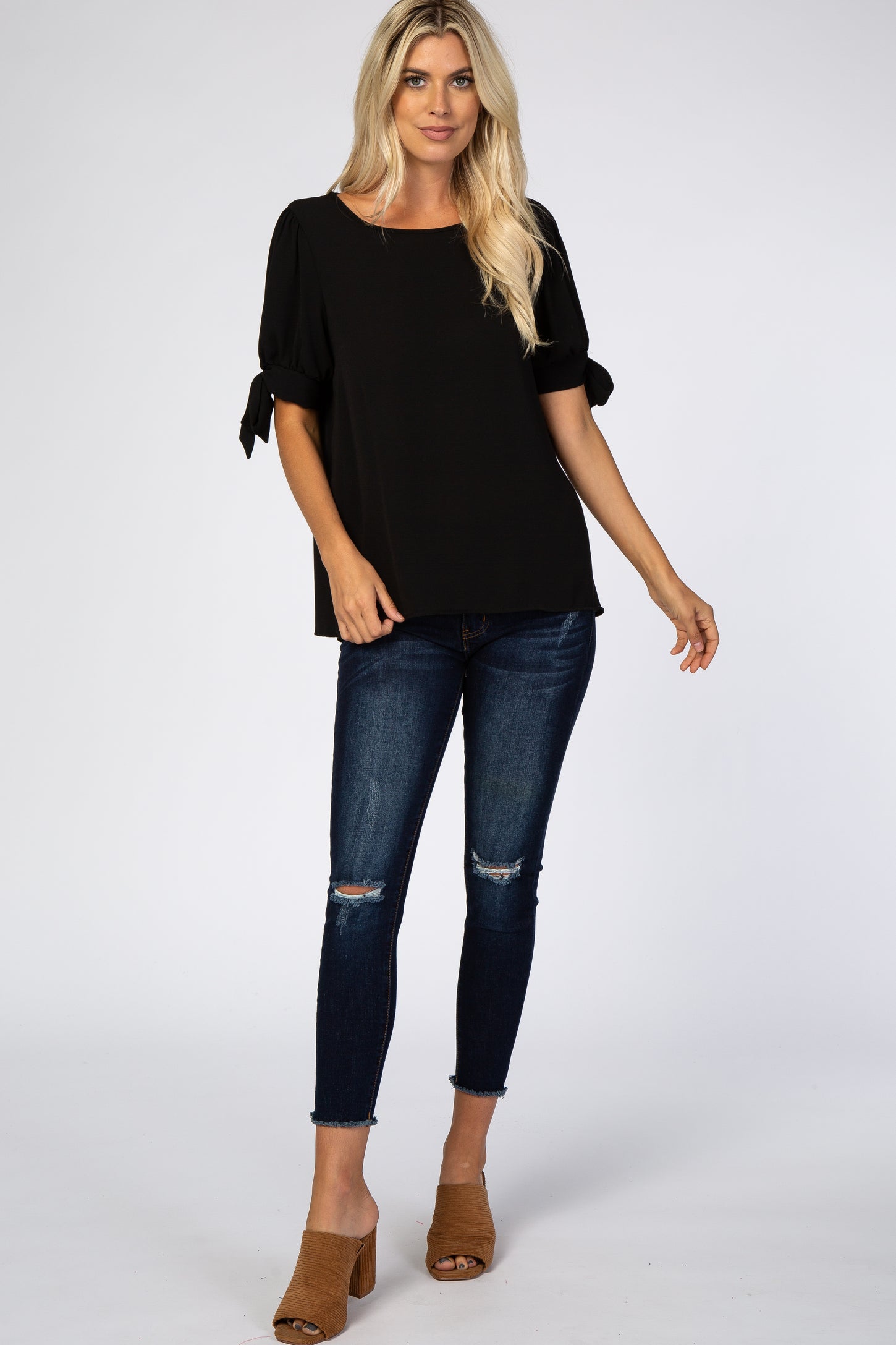 Woman wearing a black short sleeve blouse with tie details and distressed dark wash skinny jeans