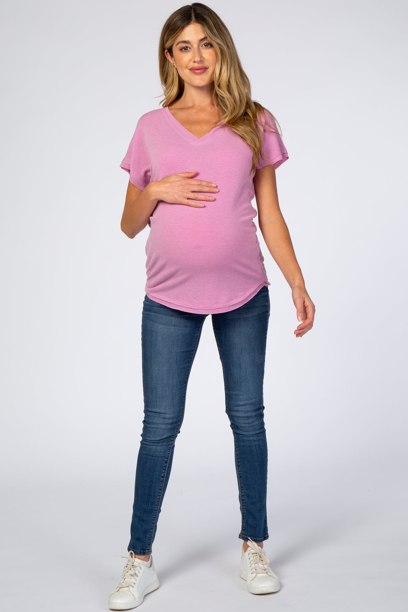 pregnant woman wearing pink v-neck maternity t-shirt and blue skinny jeans with white sneakers