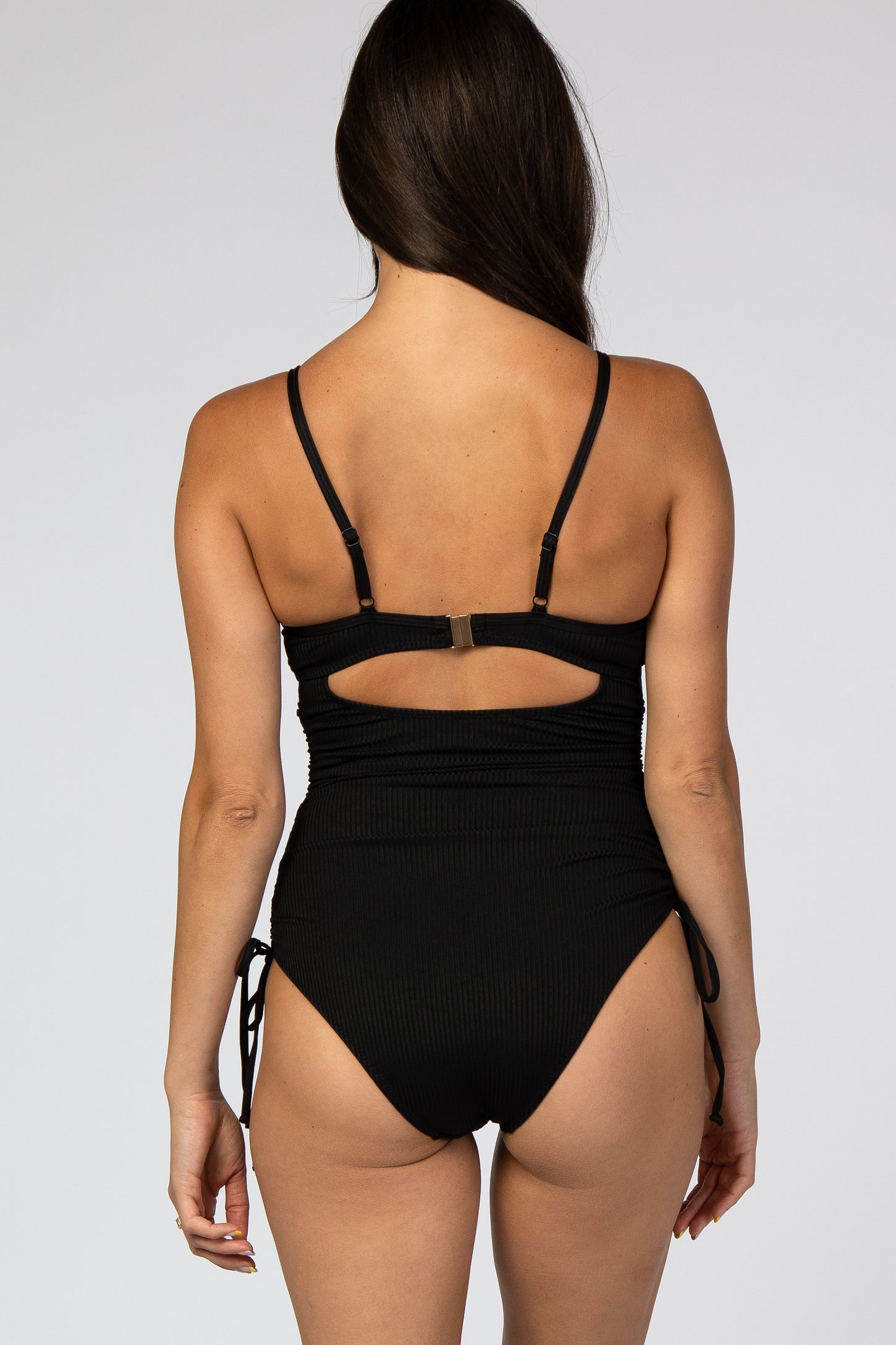 woman wearing a black ribbed one-piece swimsuit with adjustable straps and cutout back detail