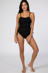 woman wearing a black ribbed one-piece swimsuit with side ties against a white background