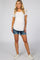 woman wearing a white short sleeve maternity t-shirt and denim shorts, showing a baby bump, standing with a smile