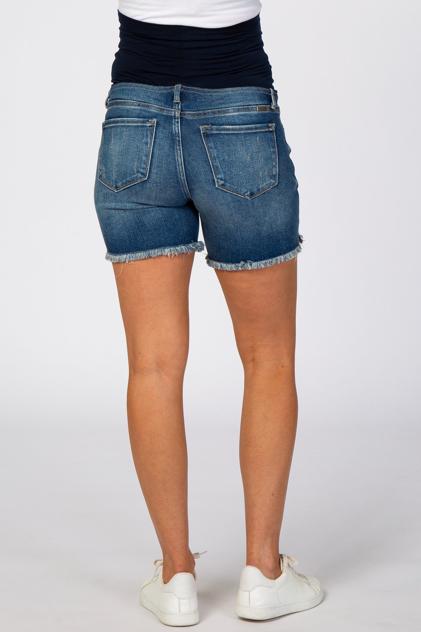 woman wearing dark blue maternity denim shorts with a fitted waistband and frayed hem, showing her legs from the back