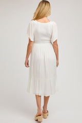 woman wearing a white maternity maxi dress with short flutter sleeves and a tiered ruffle hem, showing her back