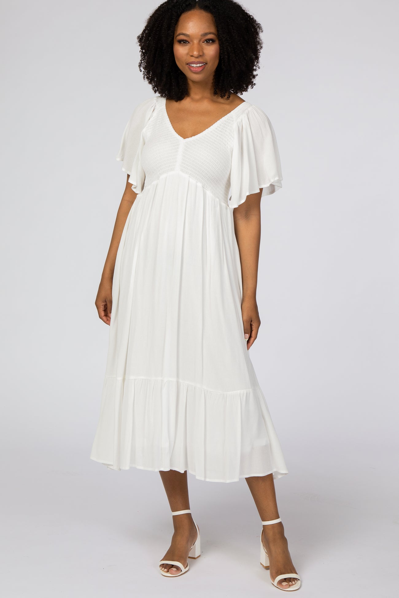 woman wearing a white midi dress with a smocked bodice and flutter sleeves, standing on a plain background