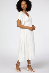 woman wearing a white midi dress with short flutter sleeves and a tiered hem, standing in profile