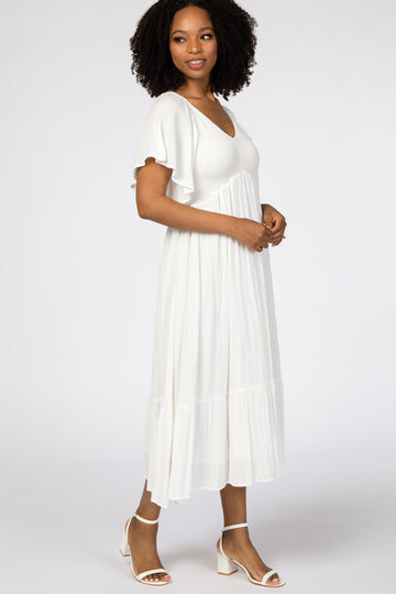 woman wearing a white midi dress with short flutter sleeves and a tiered hem, standing in profile