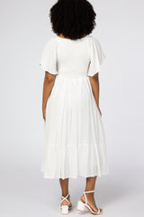 woman wearing a white midi dress with short flutter sleeves and a tiered skirt, showing the back view