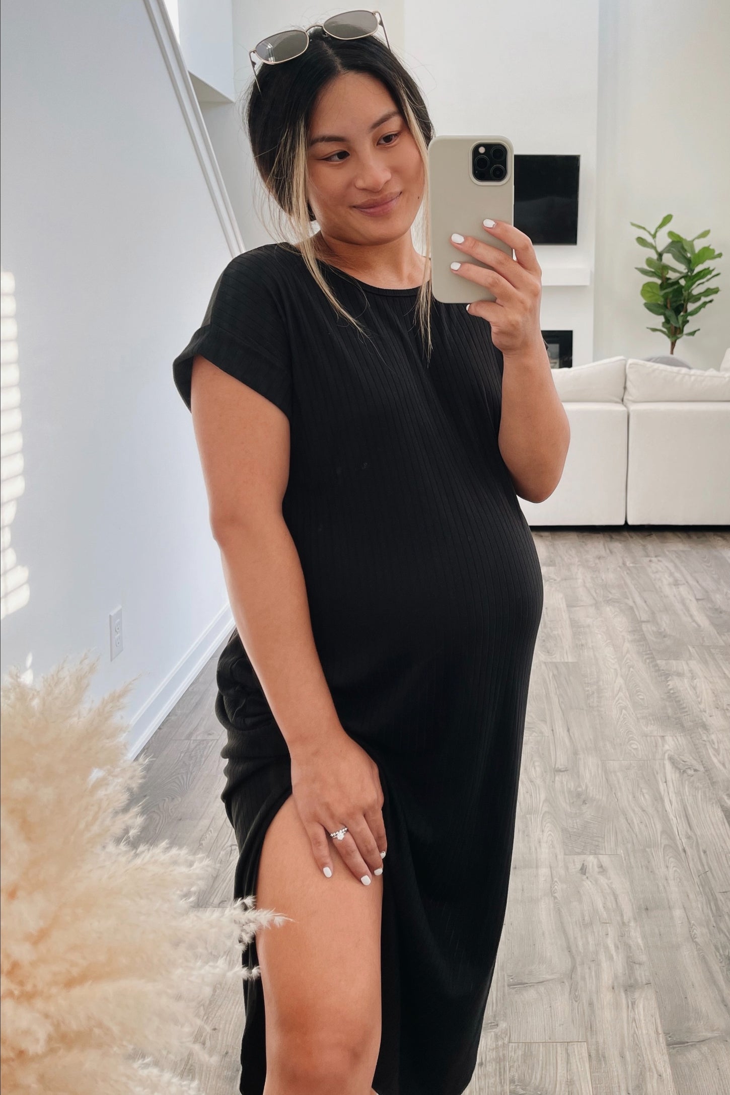 woman wearing a black short sleeve maternity dress with a side slit and holding her baby bump