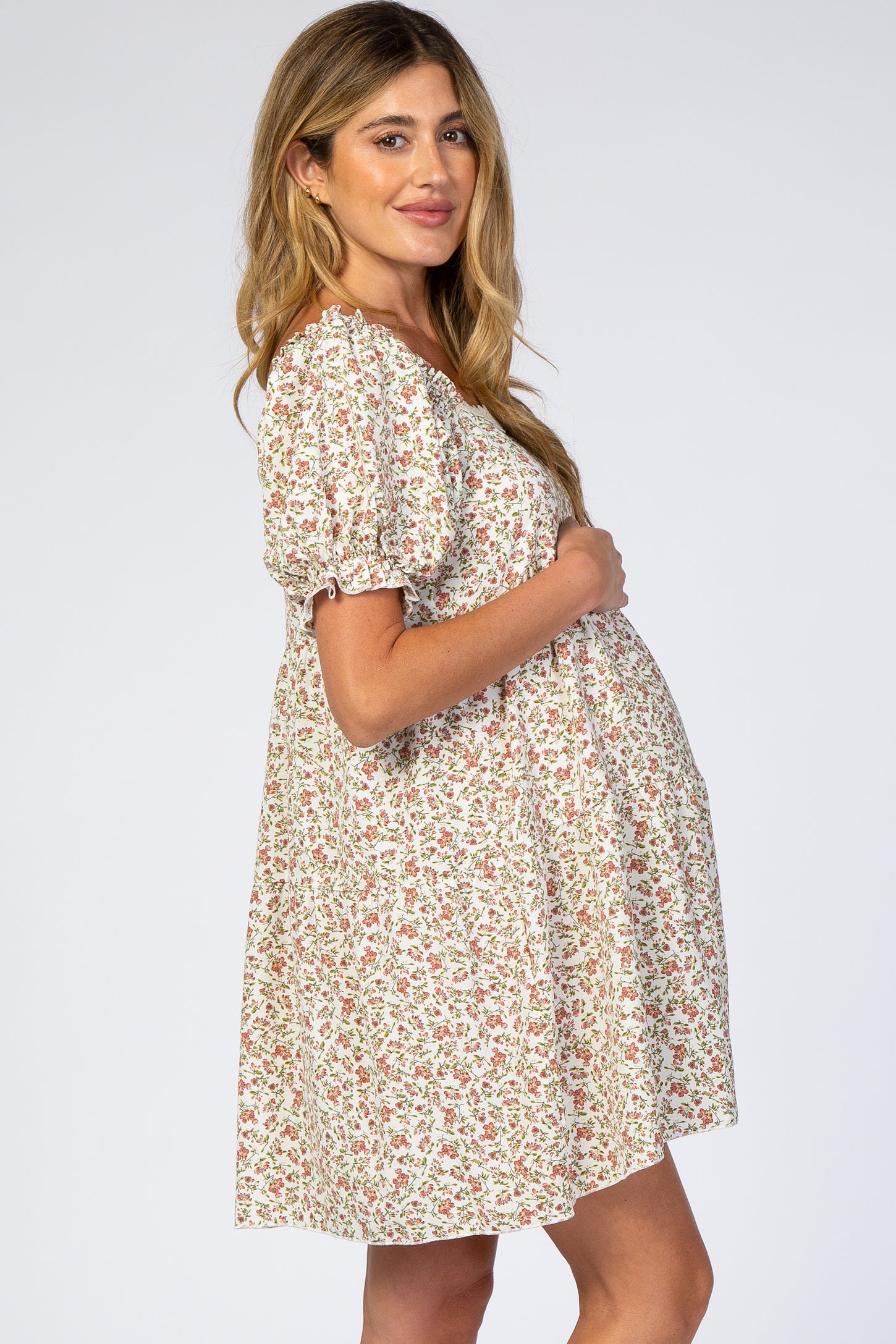 Pregnant woman in a floral puff sleeve maternity dress holding her baby bump against a white background