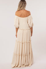 woman wearing a beige off-the-shoulder maternity dress with puff sleeves and tiered design from the back