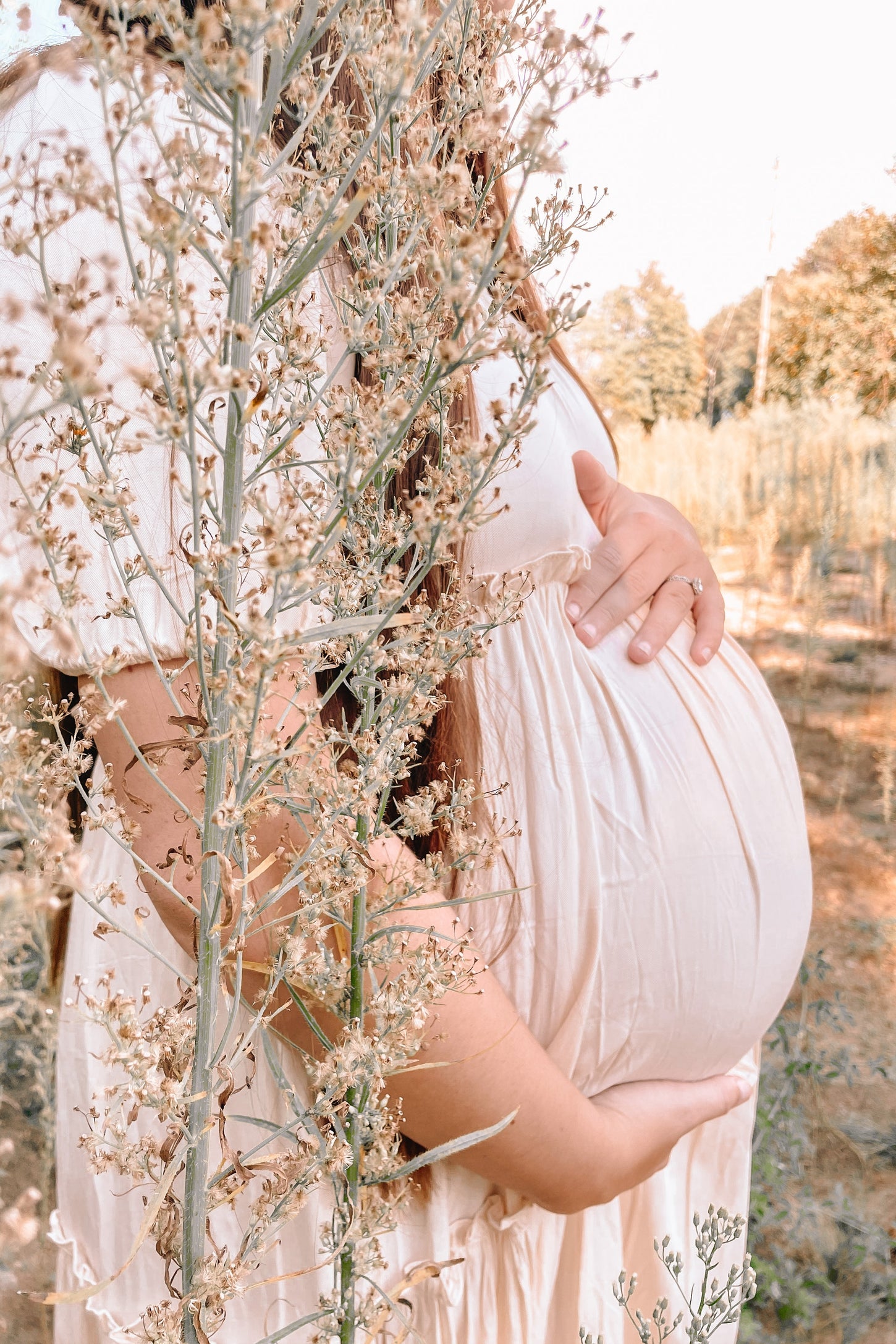 woman wearing a light pink maternity dress and holding her baby bump among plants