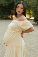 woman wearing a soft beige off-shoulder maternity dress with ruffled details and visible baby bump