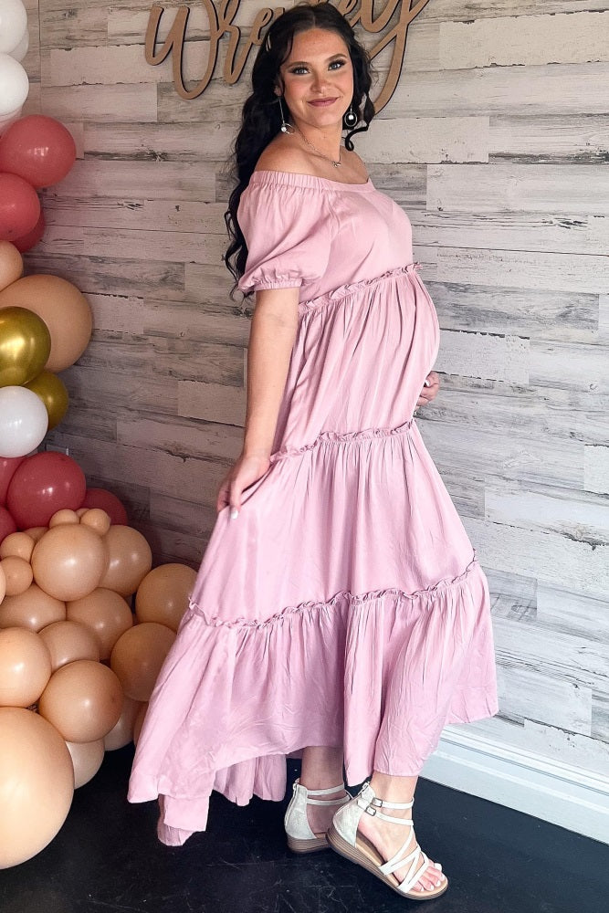 woman wearing a pink off-the-shoulder maternity dress with tiered ruffles and a visible baby bump