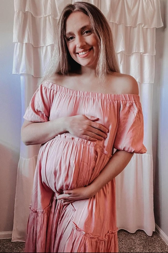 woman wearing a blush pink off-the-shoulder maternity dress and holding her baby bump
