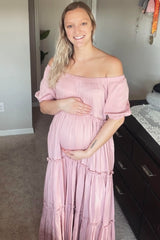 woman wearing a pink off-the-shoulder maxi dress and holding her baby bump, showcasing maternity wear