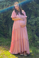 woman wearing a pink off-the-shoulder maternity maxi dress and holding her baby bump
