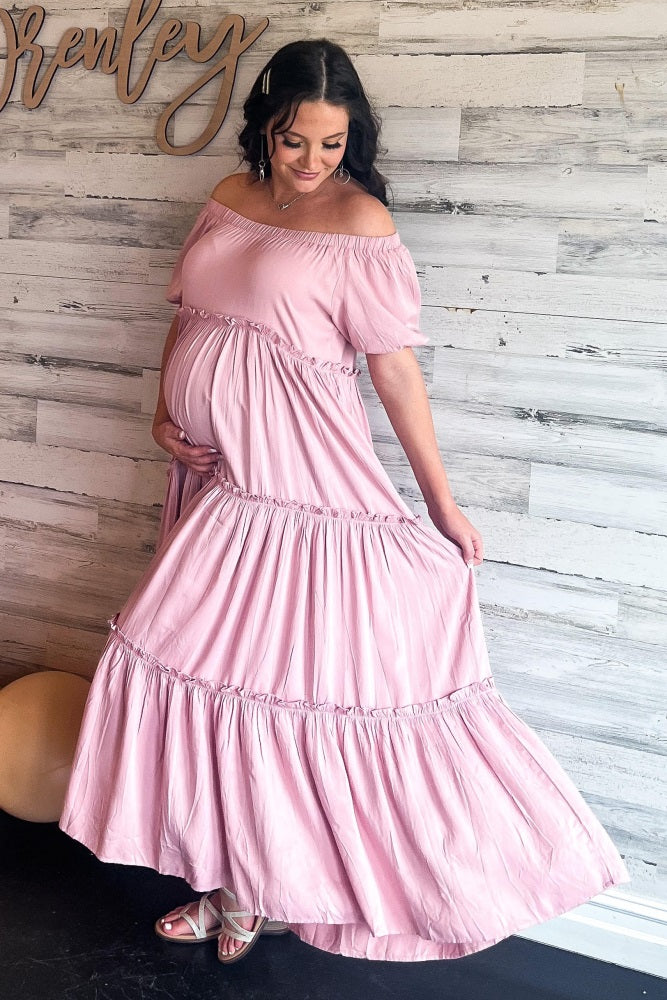 woman wearing a light pink off-shoulder maternity dress with a flowy skirt, showing her baby bump