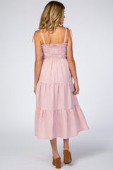 woman wearing a pink and white gingham maternity dress with tie shoulder straps and a tiered skirt, showing a baby bump