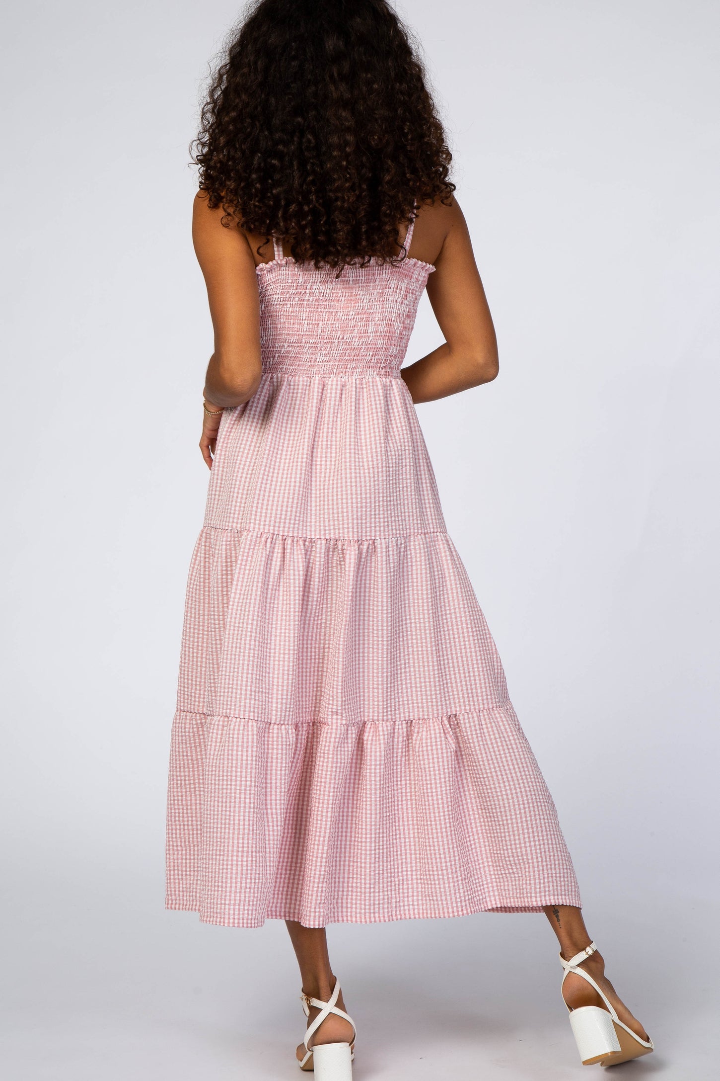 woman wearing a pink and white checked maxi dress with a smocked bodice and tiered skirt standing from the back