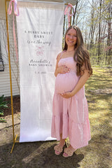 Smiling pregnant woman in pink gingham dress standing next to a berry sweet baby shower banner outdoors