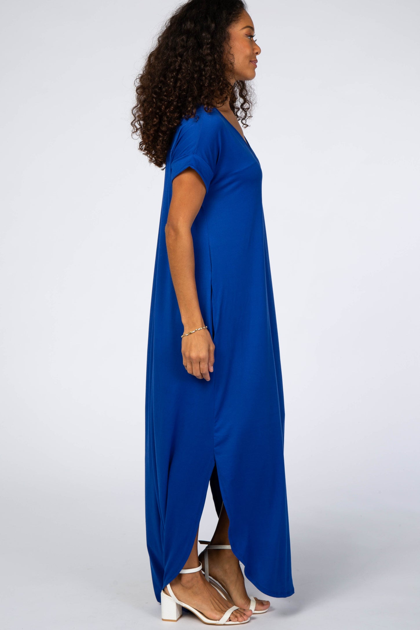 woman wearing a bright blue maxi dress with short sleeves and side slits, standing in profile with curly hair